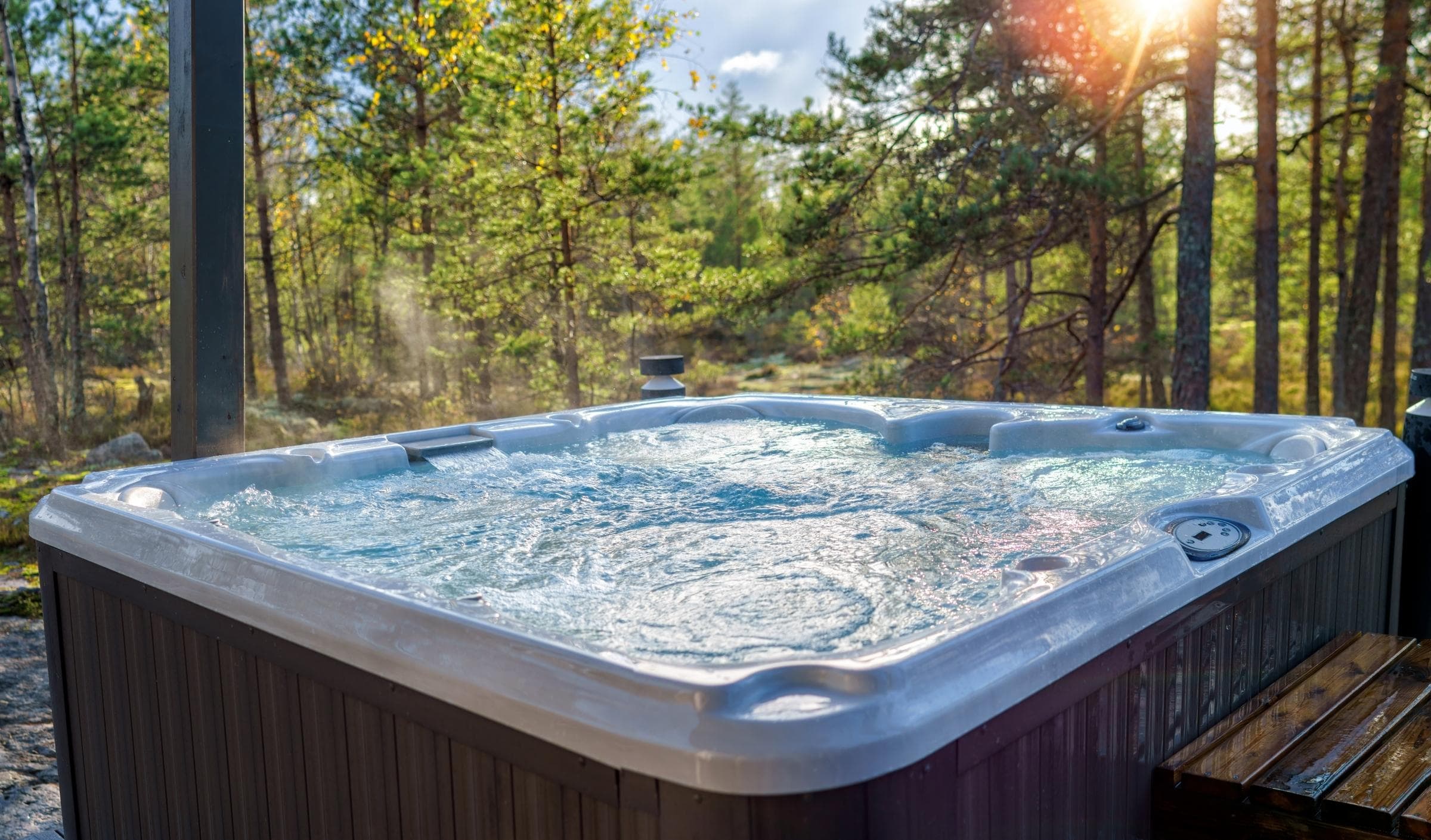 Open hot tub on a covered lakeside deck overlooking a green lawn and blue water on a sunny day